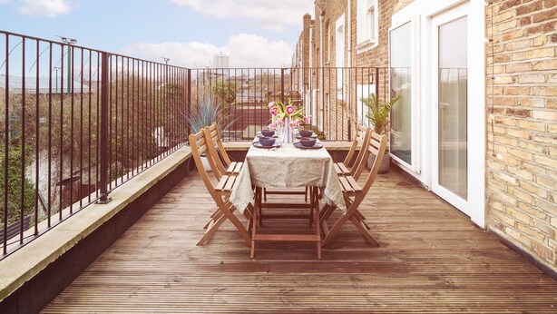 Une terrasse en bois avec une table dressée pour le repas, entourée d’immeubles en briques et d’une clôture en métal.