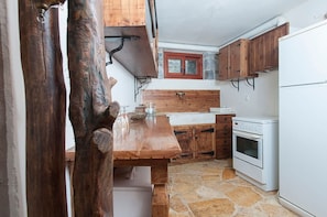 A rustic kitchen with a wooden table, stone flooring, wooden cabinets, and white appliances. - Authenticity of Living in Mani for Nature Lovers (West Mani)