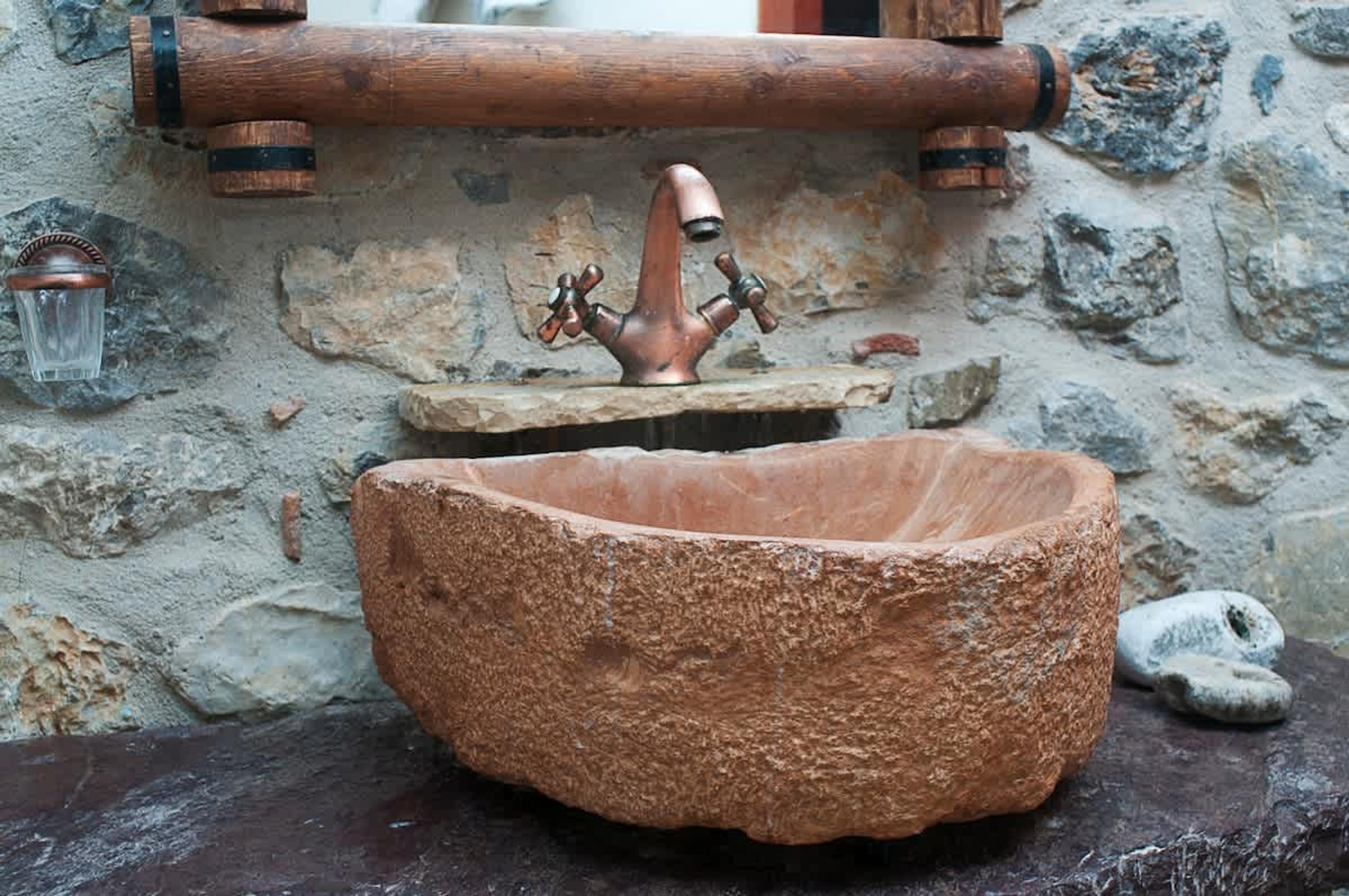 A rustic stone sink with a copper faucet and a stone basin.