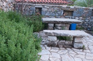 A stone bench with a blue trash bin nearby, set against a stone wall and surrounded by greenery. - Authenticity of Living in Mani for Nature Lovers (West Mani)