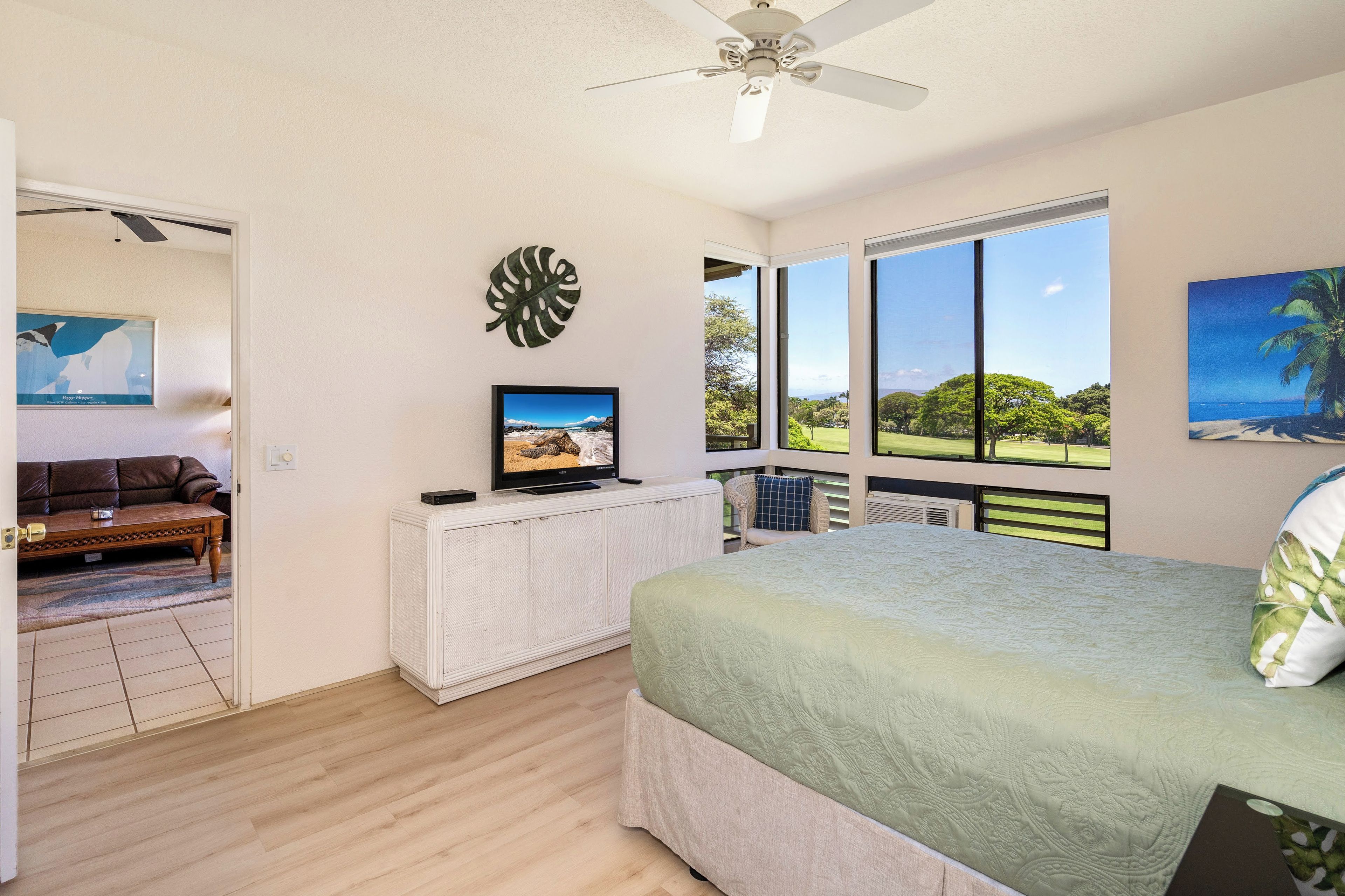Une chambre à coucher avec un lit, un téléviseur posé sur un meuble, une grande fenêtre donnant sur un beau paysage et un ventilateur de plafond.