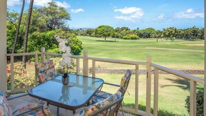 A covered outdoor seating area with a table and chairs, overlooking a golf course. - Grand Champions #147 Golf Course Views Full Kitchen AC In Bedrooms (Kihei)