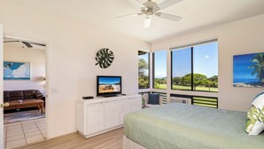 A bedroom with a bed, a television on a cabinet, a large window with a view, and a ceiling fan. - Grand Champions #147 Golf Course Views Full Kitchen AC In Bedrooms (Kihei)