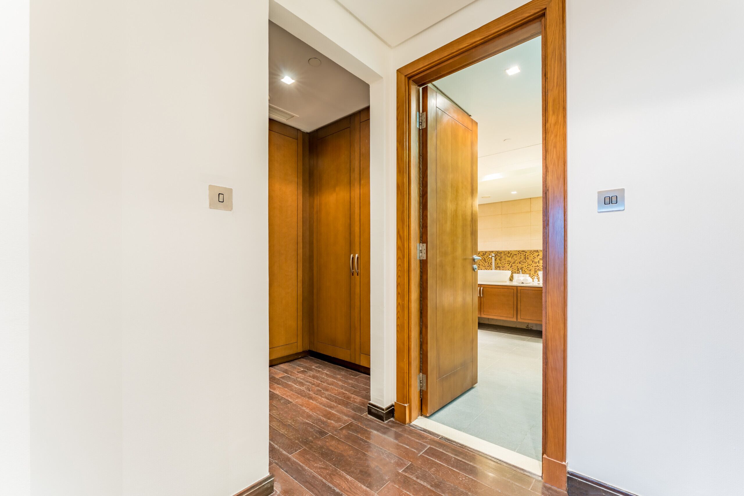A hallway with wooden doors leading to a bathroom with a sink and mirror.