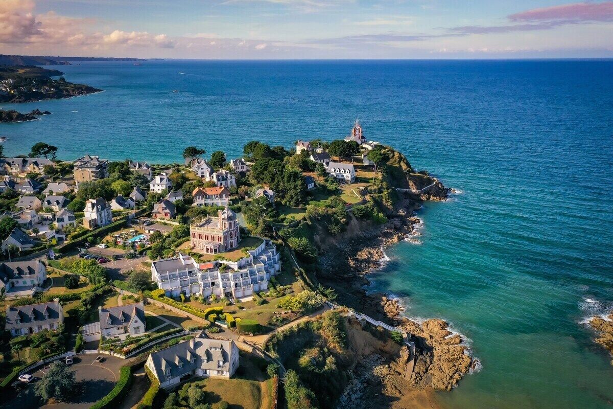 An aerial view of a coastal town with houses, a prominent church, and a rocky coastline.