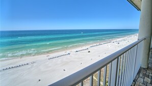 Une vue sur la plage depuis un balcon doté d’une balustrade, avec un ciel bleu dégagé et une mer calme.