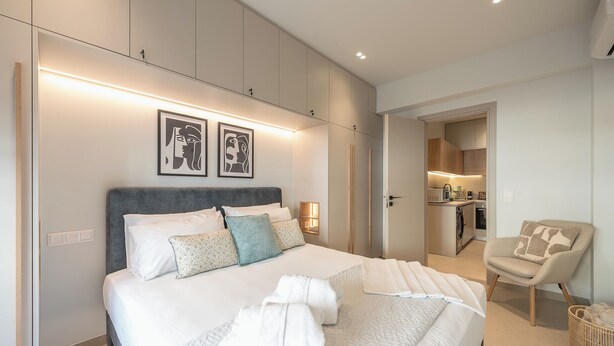 Ein modernes Schlafzimmer mit einem großen Bett, einem kleinen Schreibtisch und einer Küchenzeile im Hintergrund.