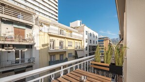 Ein Balkon mit Holzmöbeln und einer Metallschale, mit Blick auf eine Stadtlandschaft mit mehrstöckigen Gebäuden und blauem Himmel.