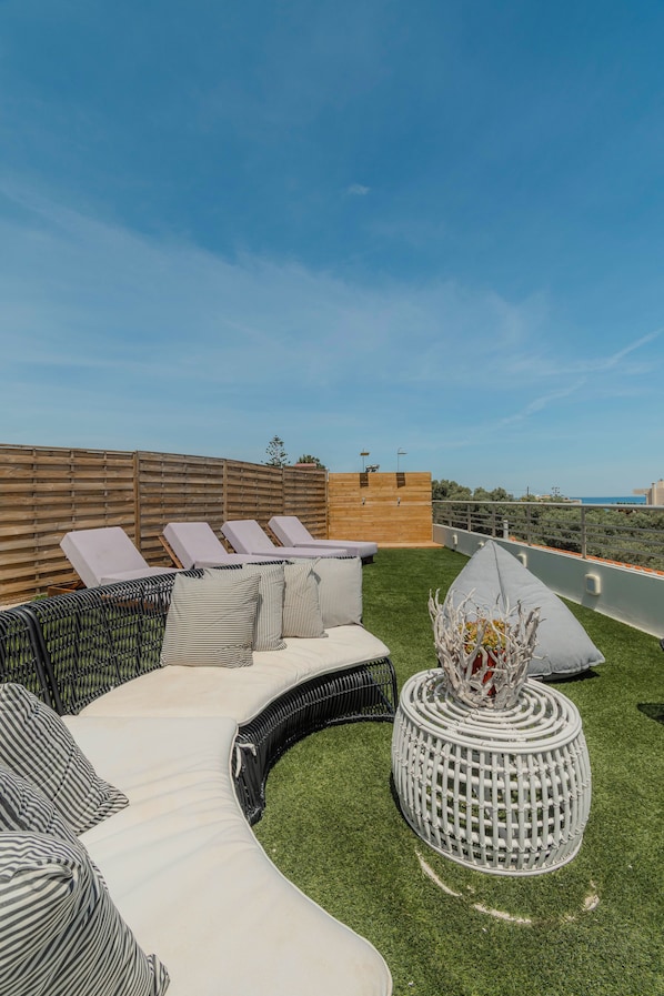 A rooftop lounge area with a curved sofa set, a round table with a decorative centerpiece, and a view of the cityscape.