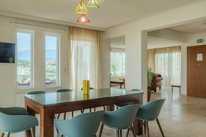 A hotel dining area with a glass-top table, teal chairs, and a view of the outdoors through large windows.