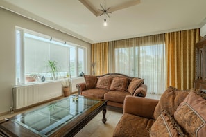 Ein Wohnzimmer mit braunen Sofas, einem Glastisch und einem großen Fenster mit Jalousien.