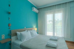 A bedroom with a bed, a bedside table, an air conditioning unit, and a window with sheer curtains.