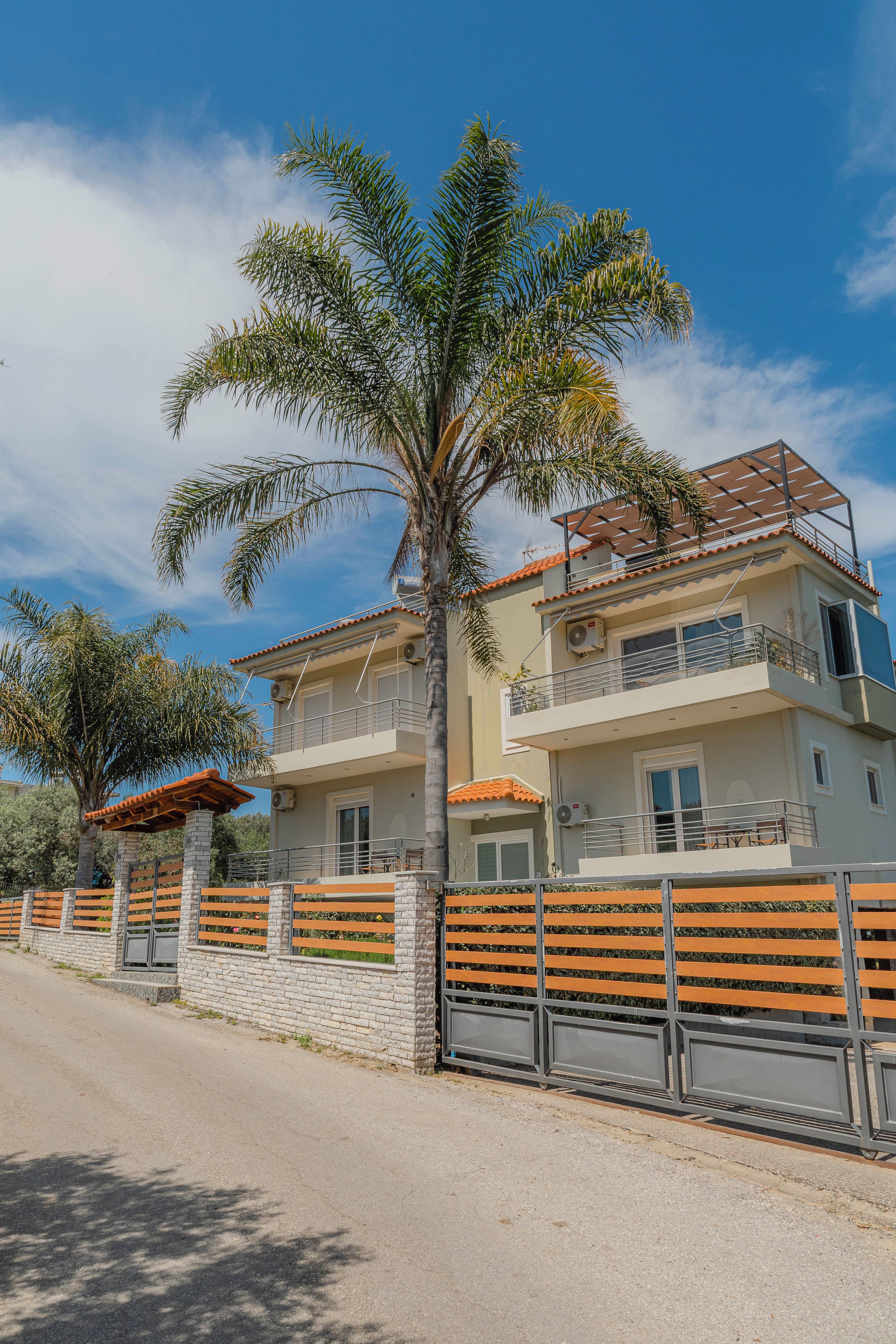 Un edificio residencial de dos pisos con un balcón, un muro de piedra y una palmera.