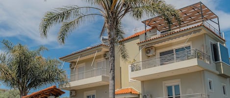 Un edificio residencial de dos pisos con un balcón, un muro de piedra y una palmera.