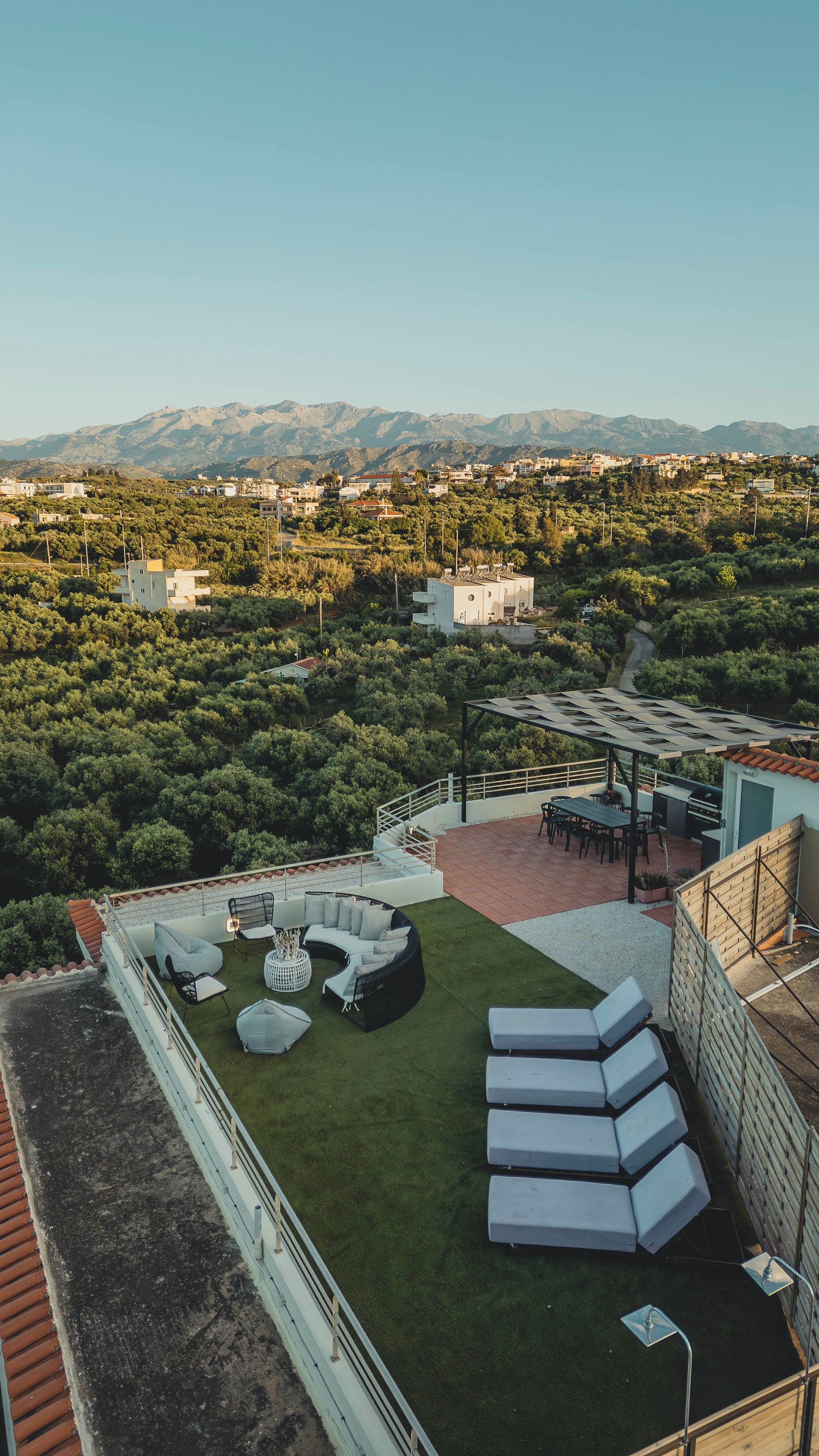 A rooftop terrace with outdoor seating, a grill, and a view of a hillside town.