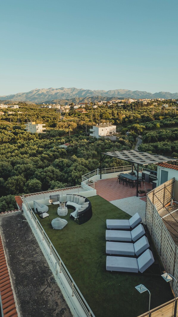 A rooftop terrace with outdoor seating, a grill, and a view of a hillside town.