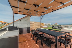 Een terras buiten met een barbecue, eettafel en stoelen.