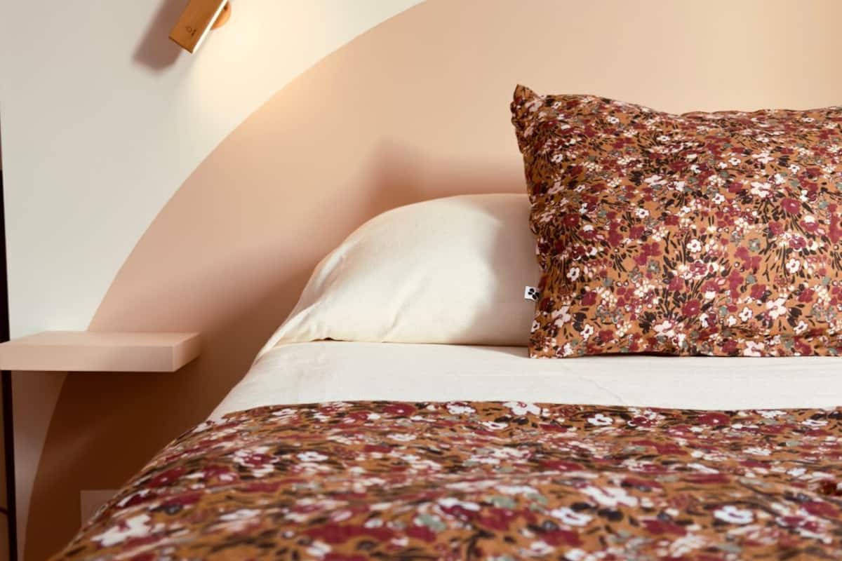 Een bed met een deken met bloemenprint, een wit kussen en een passend kussen op een hoofdbord.
