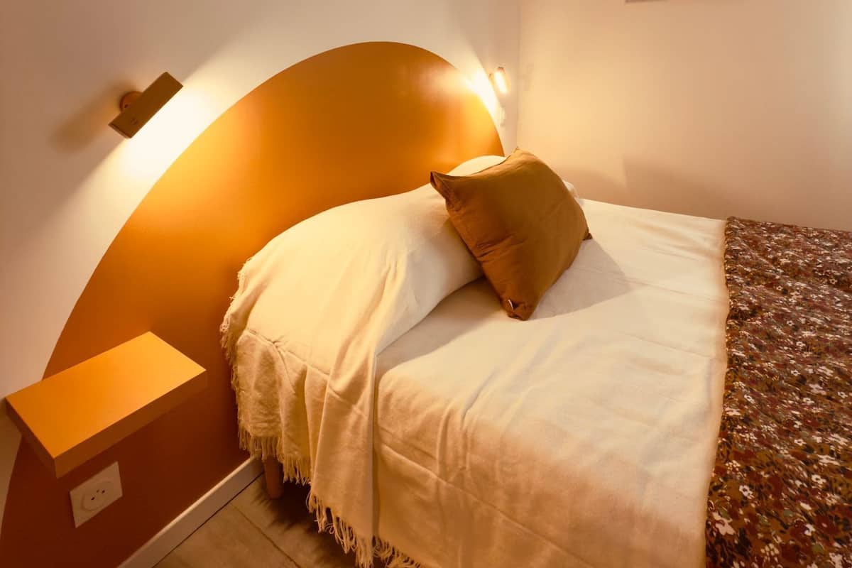 Een slaapkamer met een bed, nachtkastje, een wandlamp en een lijst met een afbeelding.