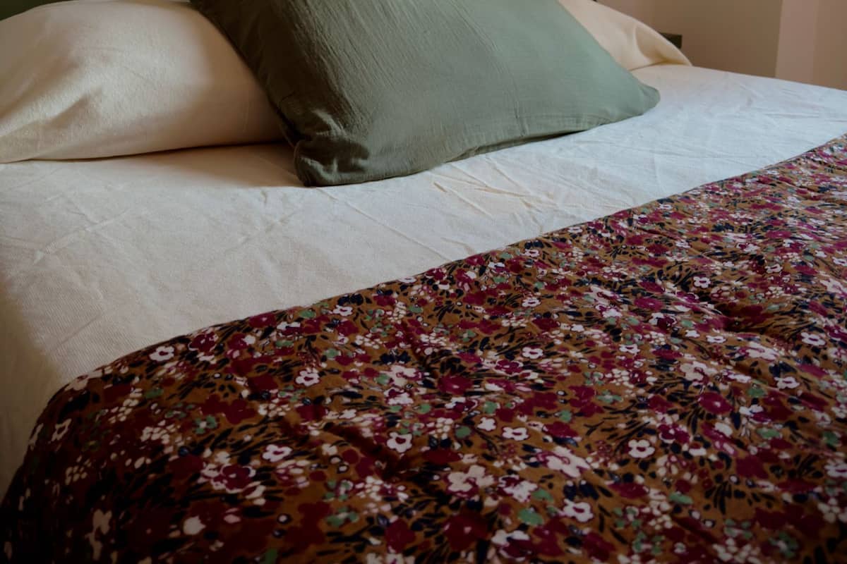 Een bed met een groen hoofdeinde, witte kussens en een bloemenprint deken.