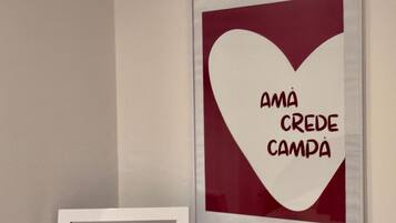 Una obra de arte enmarco con forma de corazón y el texto "Amá crede campa" sobre una pared blanca.