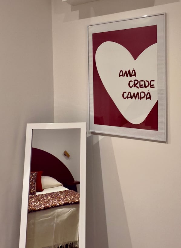 Une œuvre d’art encadrée, représentant un cœur, avec l’inscription « Amá crede campa » sur un mur blanc.