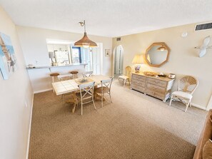 A dining area with a table and chairs, a kitchen in the background, and a decorative mirror on the wall. - Beachfront Condo | Balcony + Pool | Near Pier (Saint Augustine)