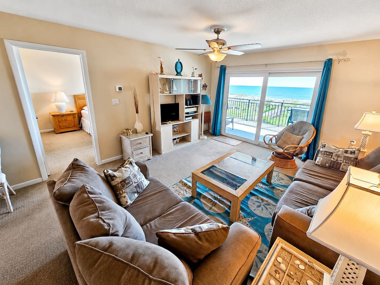 A living room with a sofa set, a coffee table, a bookshelf, and a view of the ocean through a balcony.