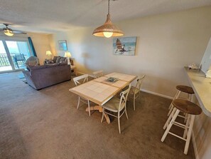 A dining area with a table and chairs, a sofa, a bar area, and a painting on the wall. - Beachfront Condo | Balcony + Pool | Near Pier (Saint Augustine)