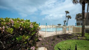 A pool area with a fence, palm trees, and a building in the background. - Beachfront Escape with Pool +Ocean & coastal Views (Saint Augustine)