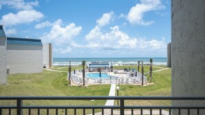 A view of a pool area with a clear sky, a building with a blue roof, and a grassy area with palm trees. - Beachfront Escape with Pool +Ocean & coastal Views (Saint Augustine)