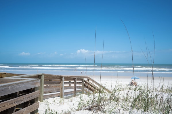 A wooden boardwalk leading to a sandy beach with ocean waves in the background.