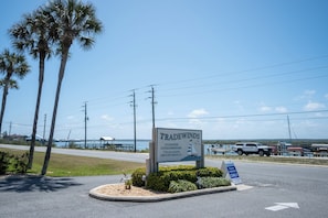 A sign for Tradewinds Oceanside Condominiums with a view of the water and palm trees.