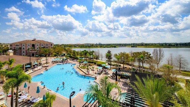A resort with a large swimming pool surrounded by palm trees and a view of a lake. - Pool View Penthouse 3 Bedroom Condo (Orlando)