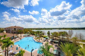A resort with a large swimming pool surrounded by palm trees and a view of a lake. - Pool View Penthouse 3 Bedroom Condo (Orlando)