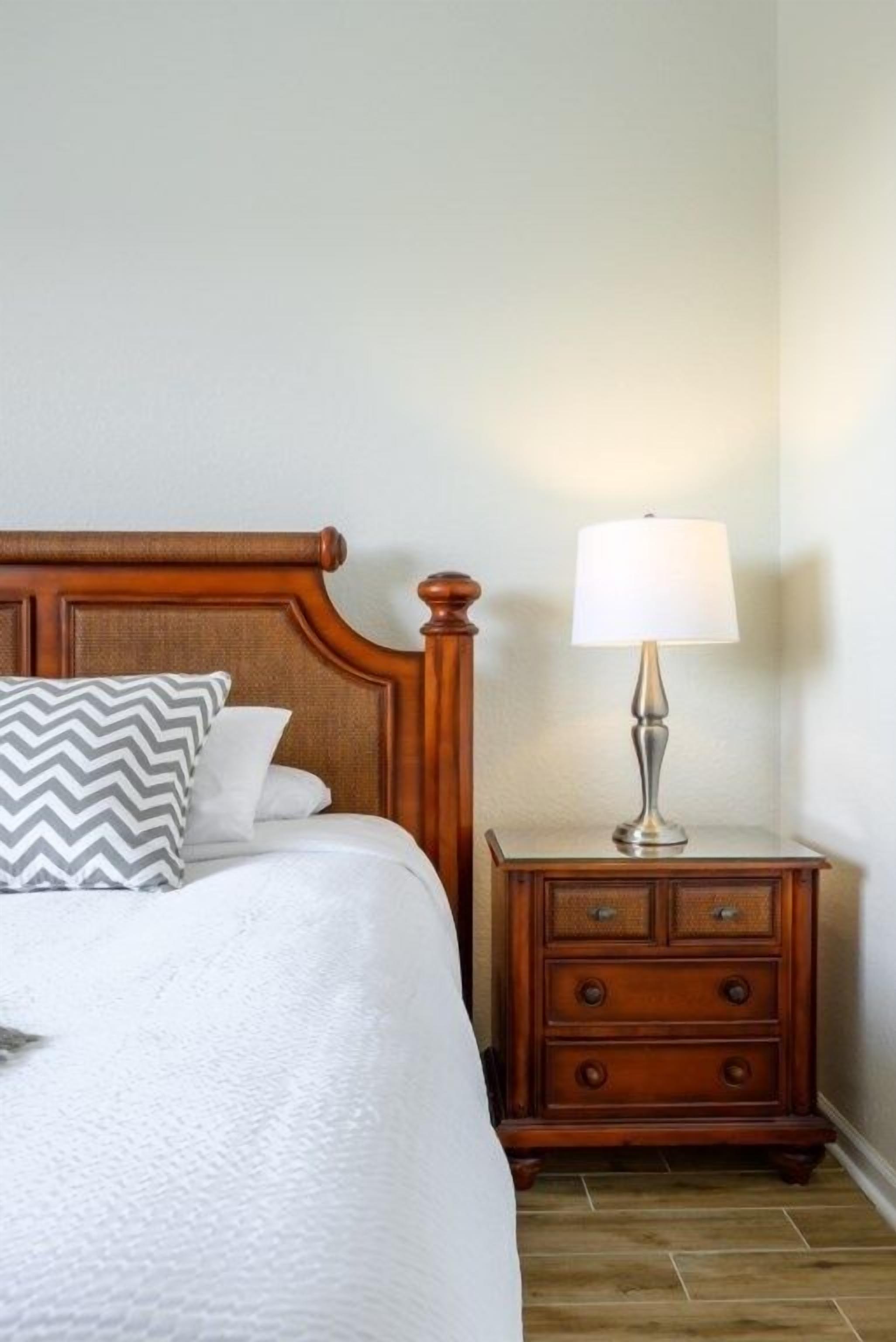 A neatly made bed with a wooden headboard, a bedside lamp, and a wooden nightstand with drawers.