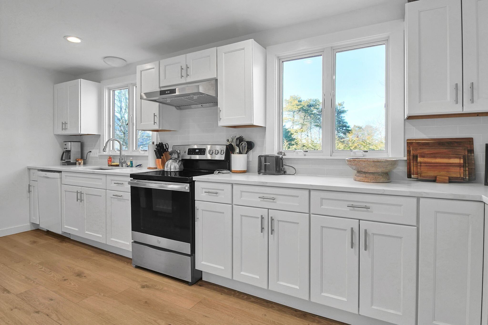 A modern kitchen with white cabinets, stainless steel appliances, and a large window providing natural light.