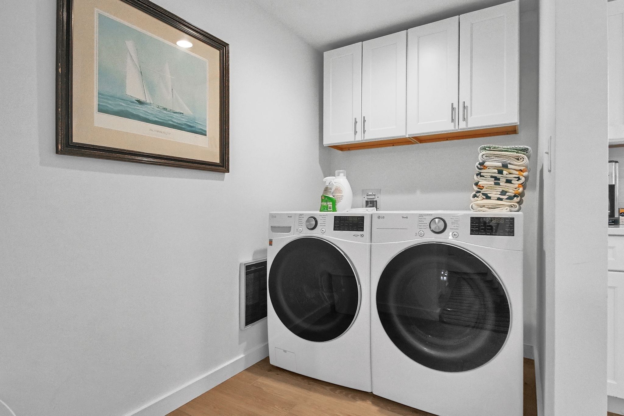 A laundry room with two front-loading washing machines, a drying rack, and a framed picture on the wall.