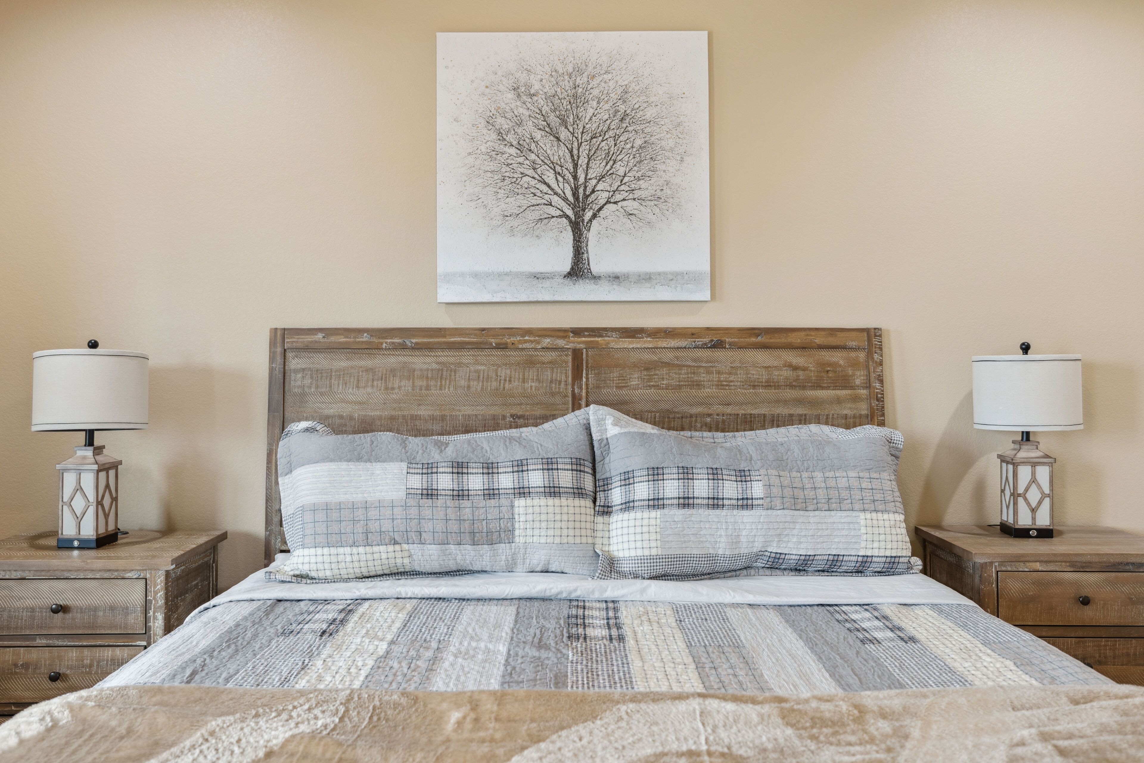A bed with a wooden headboard, two bedside tables with lamps, and a wall-mounted picture of a tree.