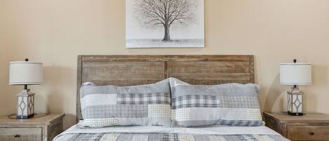 A bed with a wooden headboard, two bedside tables with lamps, and a wall-mounted picture of a tree.