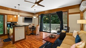 A spacious living area with a wooden floor, a ceiling fan, a kitchen island, and a balcony with outdoor furniture. - Kauai Kiahuna Plantation #425 1 Bedroom Condo (Koloa)