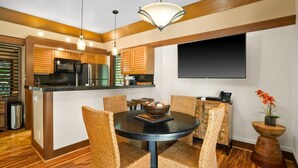 A modern kitchen with wooden cabinets, a black countertop, and a dining area with wicker chairs and a round table. - Kauai Kiahuna Plantation #425 1 Bedroom Condo (Koloa)