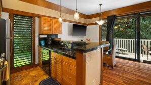 A modern kitchen with wooden cabinets, a black countertop, and pendant lighting. - Kauai Kiahuna Plantation #425 1 Bedroom Condo (Koloa)