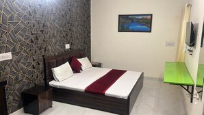 Une chambre à coucher comprenant un lit, une table de chevet, une table verte, un téléviseur et un mur orné d’un motif géométrique.