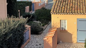 A residential area with a paved pathway, a building with a tiled roof, and a view of a hillside with houses and a body of water in the background. - 3* duplex apartment with balcony facing the sea (Sainte-Maxime)