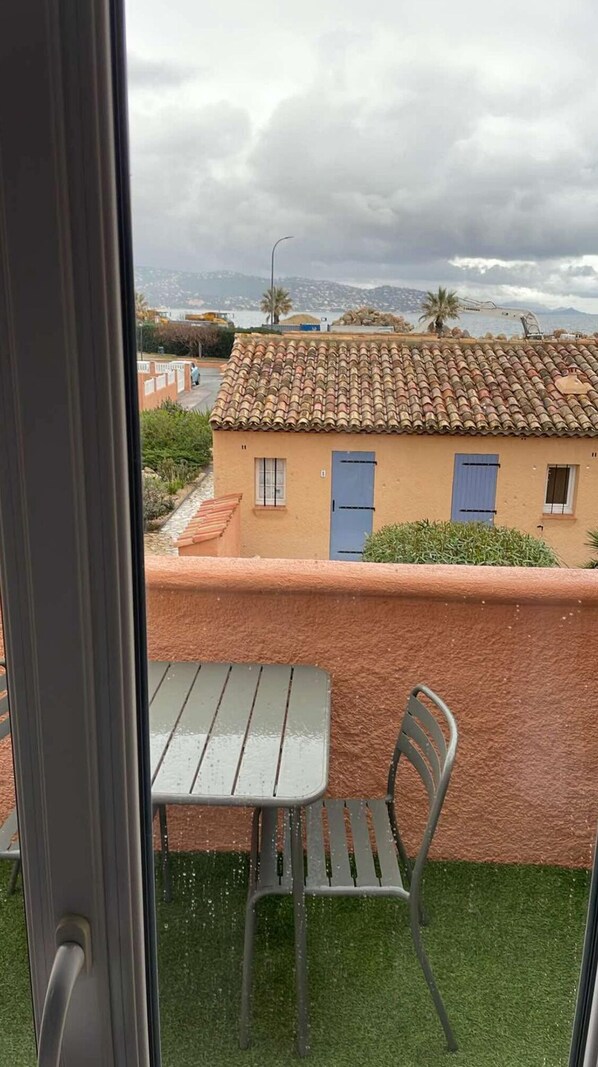 Un balcon avec une table et des chaises, une vue sur un bâtiment avec un toit en tuiles et un paysage montagneux en arrière-plan.