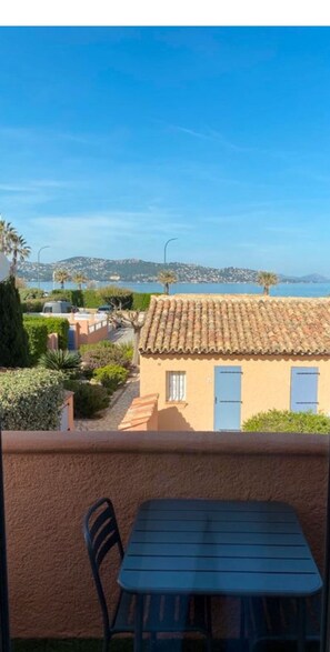 A balcony with a table and chairs, overlooking a coastal area with terracotta-roofed buildings and a clear blue sky. - 3* duplex apartment with balcony facing the sea (Sainte-Maxime)