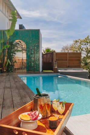 A poolside setting with a wooden deck, a pool, and a tray with drinks and fruit. - Horizonte: Villa with heated pool & jacuzzi – Wellness in Biarritz (Biarritz)