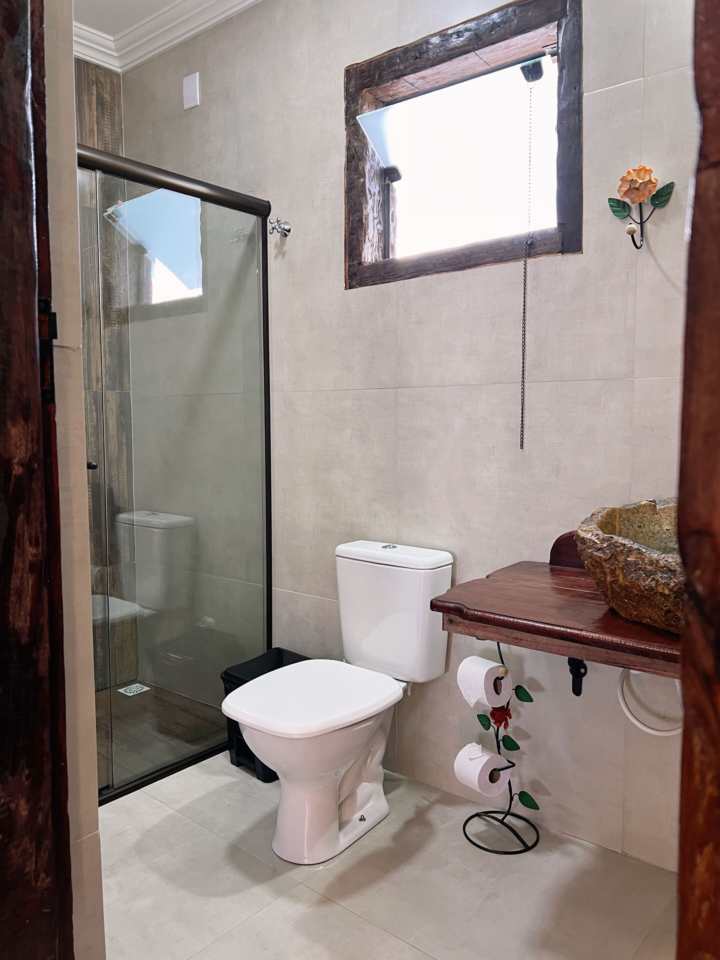 A bathroom with a glass shower enclosure, a toilet, a sink with a decorative bowl, and a wall-mounted mirror.