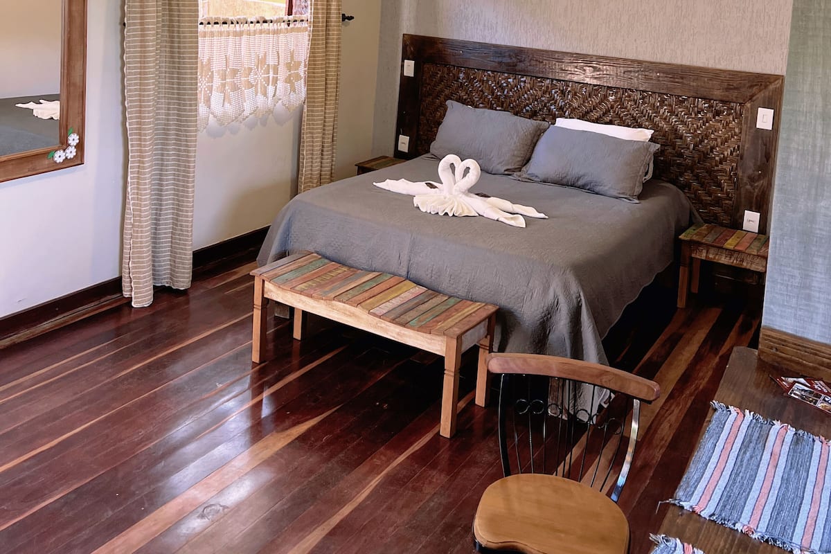 Une chambre à coucher avec un lit en bois, un banc, une chaise, une table de chevet en bois et un miroir.